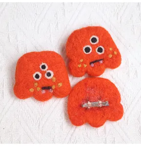 Detail showing back pin of handmade orange three-eyed monster wool felt brooch