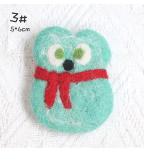 Detailed view of handmade green wool felt owl brooch with a red scarf on knit fabric