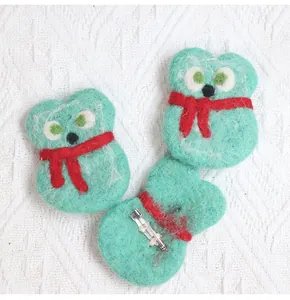 Detail of handmade green wool felt monster brooches with red scarves and metal pins