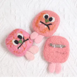 Close-up of pink wool felt monster brooches with detail of metal pin back and soft texture