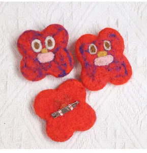 Detail of handmade red wool felt flower brooches with cute cartoon faces and metal pins