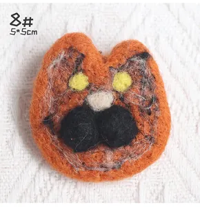 Close-up of orange wool felt cat face brooch with 5x5cm size detail on white fabric