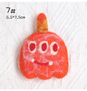 Detail of handmade orange wool felt monster brooch with three eyes and yellow crest