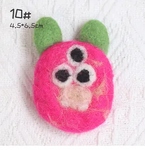 Close-up of pink three-eyed wool felt monster brooch with measurements 4.5x6.5cm