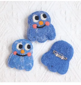 Detailed close-up showing front and back of blue wool felt monster brooches with metal pins