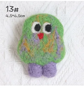 Detail of a handmade green wool felt monster brooch with big eyes and 4.5x6.5cm dimensions