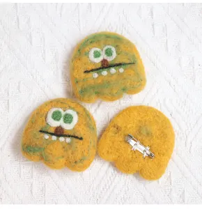Detail of yellow wool felt monster brooch showing secure silver metal safety pin attachment