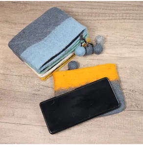 Detail view of wool felt pouch with zipper and pompom charm next to a smartphone
