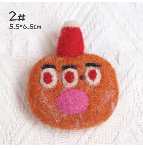 Macro detail of handmade wool felt monster brooch with red hat and triple eyes design