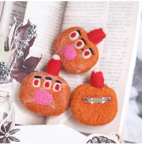Detail of three handmade wool felt monster brooches with red hats on an open book