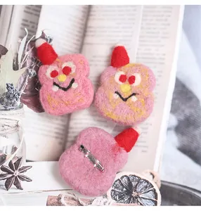 Macro detail of handmade wool felt pink monster brooches with festive red hats and pins