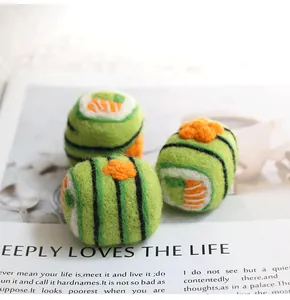 Detail of three green wool felt sushi charms on a magazine background with soft natural lighting