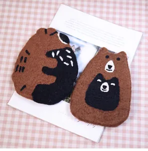 Close-up of handmade brown bear and black cat wool felt coasters on a plaid cloth