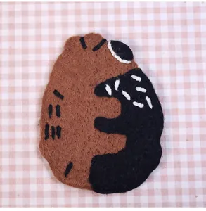 Close-up of handmade brown wool felt bear coaster on pink plaid fabric background