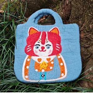 Detail of light blue felt handbag featuring a handcrafted fiber art cat character design