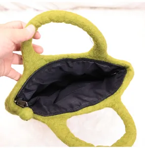 Close-up of grass green felt handbag featuring a black zipper and fluffy ball pendant