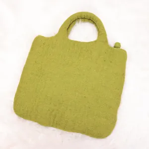 Cute avocado green felt handbag with a round ball charm on soft white plush background