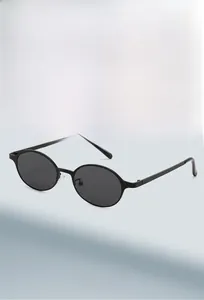 Details einer mattschwarzen ovalen Sonnenbrille mit dunklen Gläsern vor blauem Hintergrund