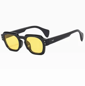Detail of chunky black polygonal frame sunglasses with bright yellow lenses and silver rivets