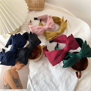 Detail view of large satin bow headbands in various colors on a soft white fabric background