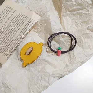 Detail of cute felt lemon clip and braided carrot pendant hair tie on white paper