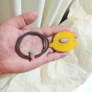 Close-up of cute cartoon yellow duck and pink carrot hair ties on hand
