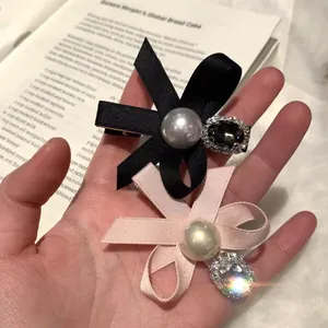 Pink and black ribbon bow hair clips with faux pearl and rhinestone accents on a book