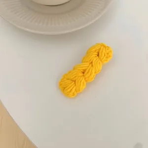 Detailopname van een handgemaakte gembergele gebreide haarclip op een witte achtergrond
