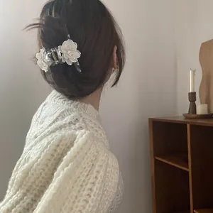 Rear view of a model wearing a clear floral hair claw clip with white flower details