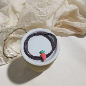 Detail of pink carrot charm on elastic purple hair tie set on white ceramic plate