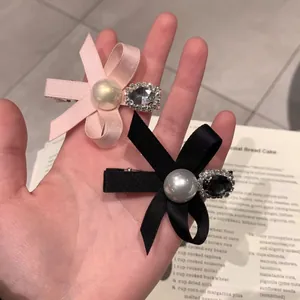 Pink and black bow hair clips with pearls and rhinestones shown on an aesthetic background