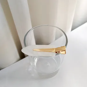 Détail d'une pince à cheveux en acétate marbré blanc avec base dorée sur un verre