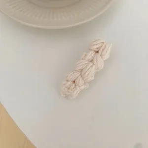 Detailopname van de crèmekleurige gebreide haarspeld met zachte garentextuur en weefsel