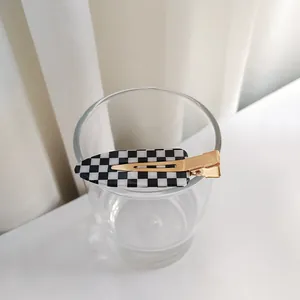 Détail de la pince à cheveux à damier avec base en métal doré sur un bord de verre
