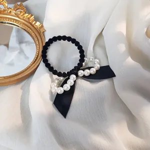 Détail d'un chouchou avec nœud en ruban noir et perles blanches sur tissu en mousseline