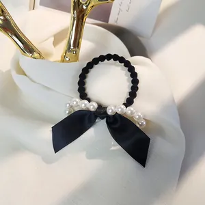 Détail d'un chouchou en satin noir avec perles blanches sur un tissu blanc doux