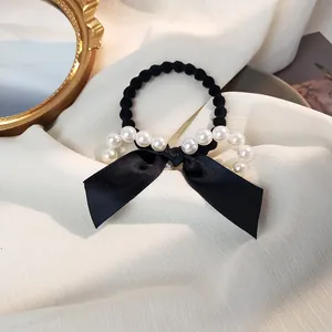 Détail de l'élastique à cheveux en satin noir avec perles blanches sur tissu plissé