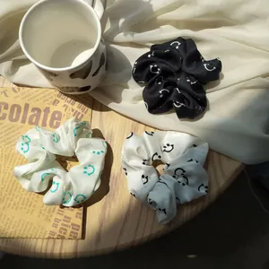 Three elegant satin scrunchies with smiley face patterns on a rustic wooden table surface