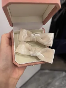 Close-up of two creamy velvet bow hair clips presented in a pink octagonal gift box