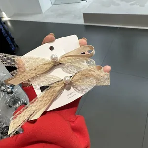 Dettaglio del fermaglio per capelli a fiocco in pizzo champagne con perla bianca