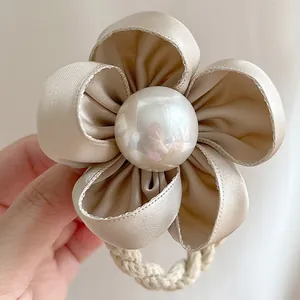Détail d'un chouchou camélia en satin champagne avec une grande perle centrale blanche