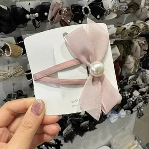 Détail d'une pince à cheveux à nœud rose clair avec perle sur carte de support