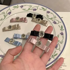 Elegant satin bow hair clip with rhinestone center shown in a stylish flatlay setting