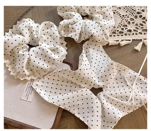 Detail of white polka dot scrunchie with lace edges and long bow tassel on wood