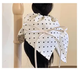 Close-up of white chiffon hair tie with black polka dots and a long cream ribbon bow