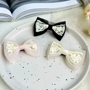 Three elegant French lace bow hair clips in black, pink and cream on a ceramic tray