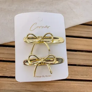 Elegant gold metal bow hair clip set for women on white display card with warm wooden background