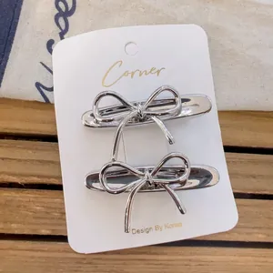 Minimalist silver metal bow hair clips on display card with a rustic wood background