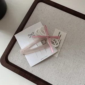 Pink velvet hair clip with white pearls and bow detail on a display card for styling