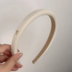 Détail d'un serre-tête en peluche beige avec logo Y en métal doré et doublure antidérapante